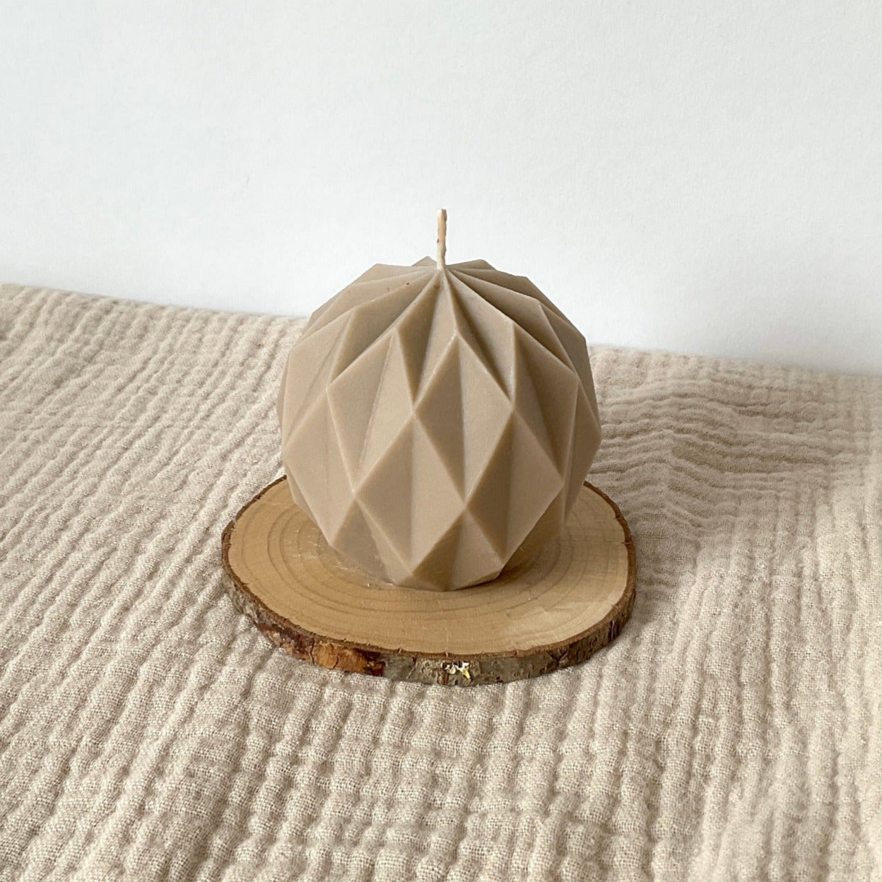 Beigefarbene geometrische Kugelkerze aus Rapswachs auf einem kleinen Holzteller.