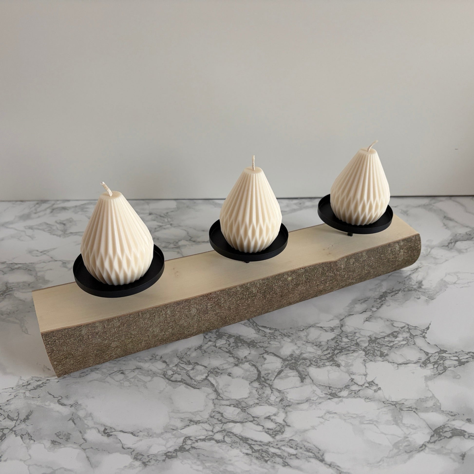 Holzstamm mit drei schwarzen Kerzentellern und 3 weißen Laternenkerzen dekoriert.